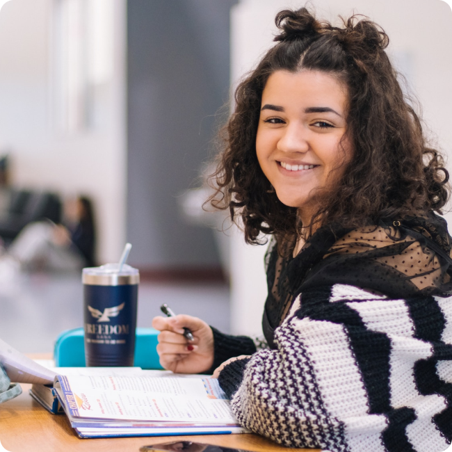 student with notebook and smiling at camera